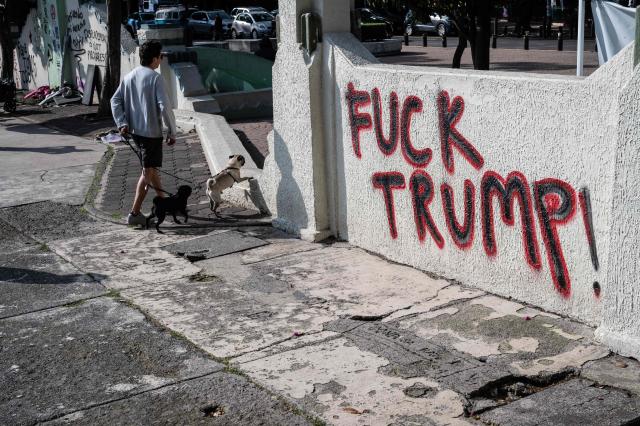 A man walks his dogs past graffiti painted by protesters a day after a march against gentrification and the increasing presence of US citizens in the La Condesa neighbourhood of Mexico City on July 5, 2025. Shouting "gringos out!" and waving banners and vandalizing various businesses, hundreds of people demonstrated this Friday in Mexico City against the gentrification of various neighborhoods due to the arrival of foreigners. (Photo by Yuri CORTEZ / AFP)