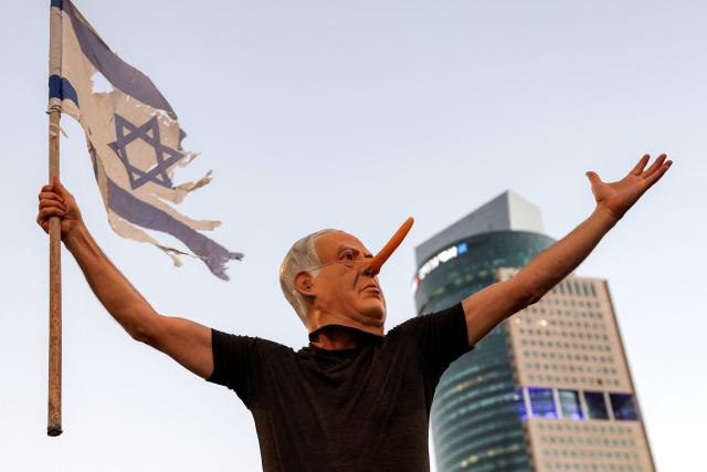 TOPSHOT - wearing a mask depicting Israeli Prime Minister Benjamin Netanyahu with an elongated nose, evoking the literary character Pinocchio, poses during an anti-government protest calling for action to secure the release of Israeli hostages held captive in the Gaza Strip by Palestinian militants since the 2023 October 7 attacks, outside the Israeli Defence Ministry headquarters in Tel Aviv on July 5, 2025. (Photo by Jack GUEZ / AFP)
