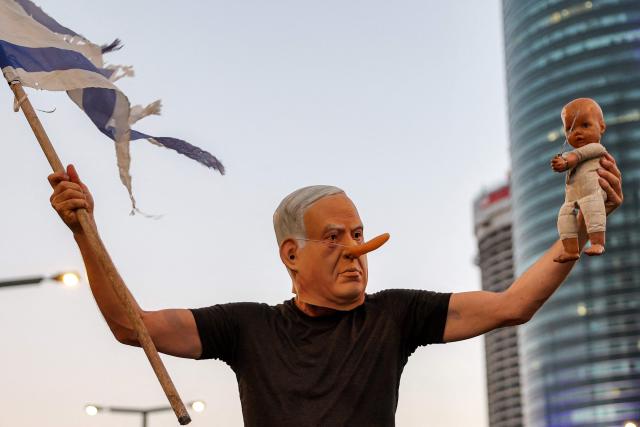 wearing a mask depicting Israeli Prime Minister Benjamin Netanyahu with an elongated nose, evoking the literary character Pinocchio, poses during an anti-government protest calling for action to secure the release of Israeli hostages held captive in the Gaza Strip by Palestinian militants since the 2023 October 7 attacks, outside the Israeli Defence Ministry headquarters in Tel Aviv on July 5, 2025. (Photo by Jack GUEZ / AFP)