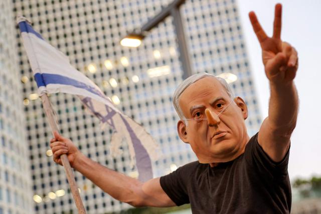 TOPSHOT - wearing a mask depicting Israeli Prime Minister Benjamin Netanyahu with an elongated nose, evoking the literary character Pinocchio, poses during an anti-government protest calling for action to secure the release of Israeli hostages held captive in the Gaza Strip by Palestinian militants since the 2023 October 7 attacks, outside the Israeli Defence Ministry headquarters in Tel Aviv on July 5, 2025. (Photo by Jack GUEZ / AFP)