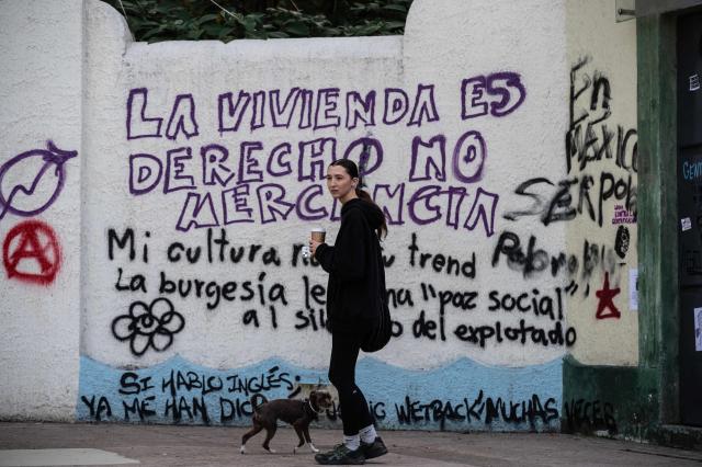 A woman walks past a wall with graffiti a day after a march against gentrification and the increasing presence of US citizens in the La Condesa neighbourhood of Mexico City at Mexico Park on July 5, 2025. Shouting "gringos out!" and waving banners and vandalizing various businesses, hundreds of people demonstrated this Friday in Mexico City against the gentrification of various neighborhoods due to the arrival of foreigners. (Photo by Yuri CORTEZ / AFP)