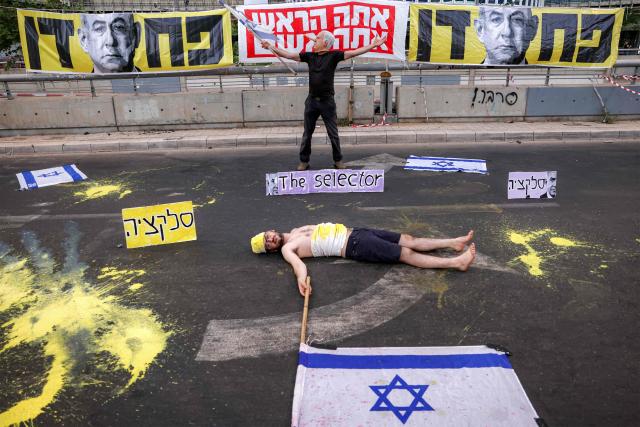 A demonstrator wearing a mask depicting Israeli Prime Minister Benjamin Netanyahu with an elongated nose, evoking the literary character Pinocchio, poses near another lying on the ground while depicting an Israeli hostage during an anti-government protest calling for action to secure the release of Israeli hostages held captive in the Gaza Strip by Palestinian militants since the 2023 October 7 attacks, outside the Israeli Defence Ministry headquarters in Tel Aviv on July 5, 2025. (Photo by Jack GUEZ / AFP)