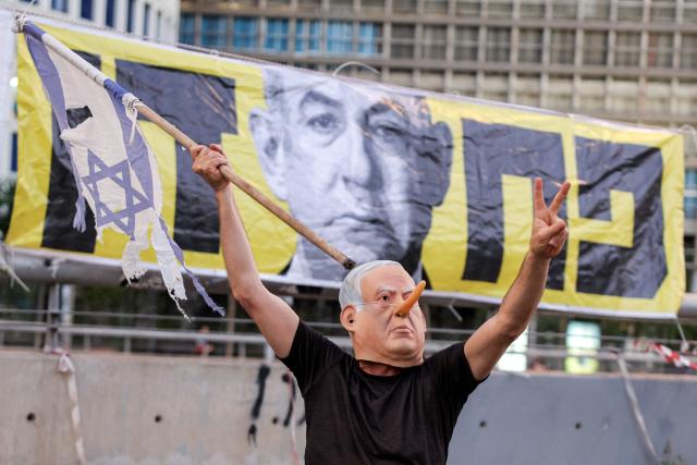 TOPSHOT - wearing a mask depicting Israeli Prime Minister Benjamin Netanyahu with an elongated nose, evoking the literary character Pinocchio, poses during an anti-government protest calling for action to secure the release of Israeli hostages held captive in the Gaza Strip by Palestinian militants since the 2023 October 7 attacks, outside the Israeli Defence Ministry headquarters in Tel Aviv on July 5, 2025. (Photo by Jack GUEZ / AFP)