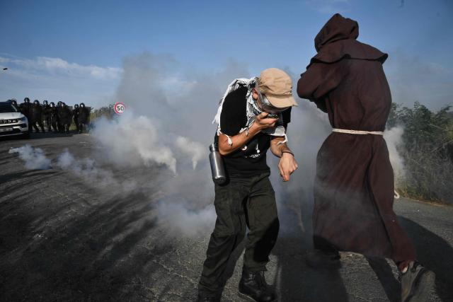 TOPSHOT - A protestor protects his face from a teargas round back towards police as protestors clash with police during a demonstration dubbed "Turbo-Teuf" against the A69 motorway project, in Morens-Scopont, southern France, on July 5, 2025. Environmental groups are holding a protest in the Tarn deparment against the construction of the Toulouse-Castres A69 motorway, despite the gathering's ban by authorities. (Photo by Ed JONES / AFP)