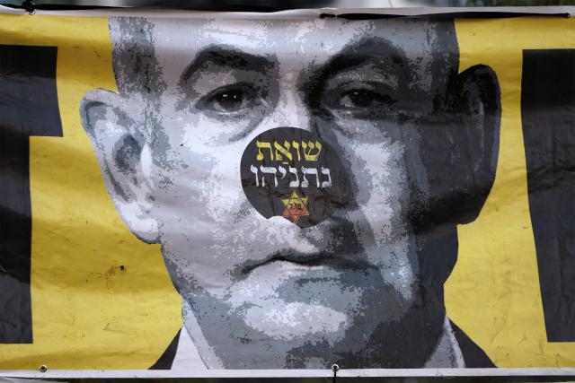 A sticker reading in Hebrew "Netanyahu's Holocaust" is displayed above a banner depicting the Israeli prime minister during an anti-government protest calling for action to secure the release of Israeli hostages held captive in the Gaza Strip by Palestinian militants since the 2023 October 7 attacks, outside the Israeli Defence Ministry headquarters in Tel Aviv on July 5, 2025. (Photo by Jack GUEZ / AFP)