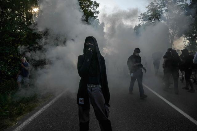 Protesters react to teargas as they clash with police during a demonstration dubbed "Turbo-Teuf" against the A69 motorway project, in Morens-Scopont, southern France, on July 5, 2025. Environmental groups are holding a protest in the Tarn deparment against the construction of the Toulouse-Castres A69 motorway, despite the gathering's ban by authorities. (Photo by Ed JONES / AFP)