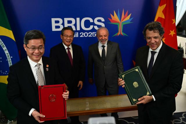 China's Finance Minister Lan Fo'an (L) and Brazil's Economy Minister Fernando Haddad pose for a picture next to China's Premier Li Qiang and Brazil's President Luiz Inacio Lula da Silva after signing a bilateral agreement, in the sidelines of the BRICS summit in Rio de Janeiro, Brazil, on July 5, 2025. BRICS leaders meeting in Rio de Janeiro from Sunday are expected to decry Donald Trump's hardline trade policies, but are struggling to bridge divides over crises roiling the Middle East. (Photo by Pablo PORCIUNCULA / AFP)