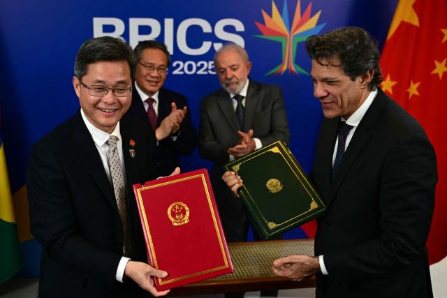 China's Finance Minister Lan Fo'an (L) and Brazil's Economy Minister Fernando Haddad pose for a picture next to China's Premier Li Qiang and Brazil's President Luiz Inacio Lula da Silva after signing a bilateral agreement, in the sidelines of the BRICS summit in Rio de Janeiro, Brazil, on July 5, 2025. BRICS leaders meeting in Rio de Janeiro from Sunday are expected to decry Donald Trump's hardline trade policies, but are struggling to bridge divides over crises roiling the Middle East. (Photo by Pablo PORCIUNCULA / AFP)