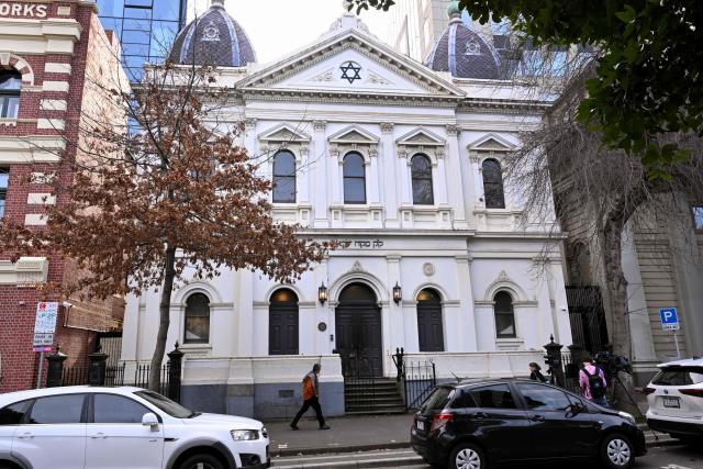 People pass the burnt front entrance of the East Melbourne Synagogue in Melbourne on July 6, 2025. A man suspected of setting fire to an Australian synagogue as worshippers ate dinner inside has been arrested and charged, police said on July 6. (Photo by William WEST / AFP)