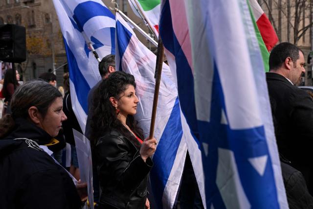 People holding the flag of Israel listen to speeches at a rally in Melbourne on July 6, 2025, after the front door of a synagogue was set ablaze on July 4. A man suspected of setting fire to an Australian synagogue as worshippers ate dinner inside has been arrested and charged, police said on July 6. (Photo by William WEST / AFP)