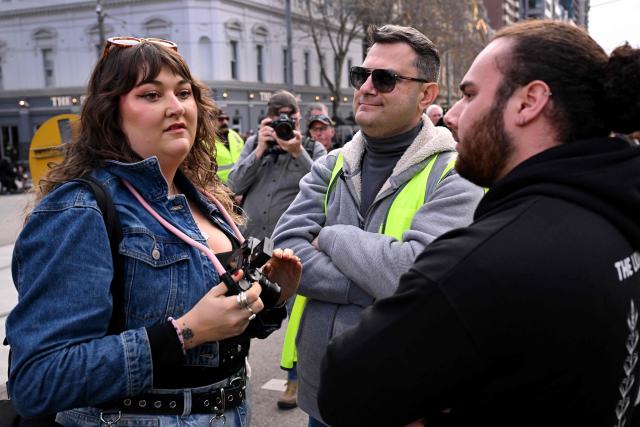 Local Israeli security block a photographer at a rally in Melbourne on July 6, 2025, after the front door of a synagogue was set ablaze on July 4. A man suspected of setting fire to an Australian synagogue as worshippers ate dinner inside has been arrested and charged, police said on July 6. (Photo by William WEST / AFP)