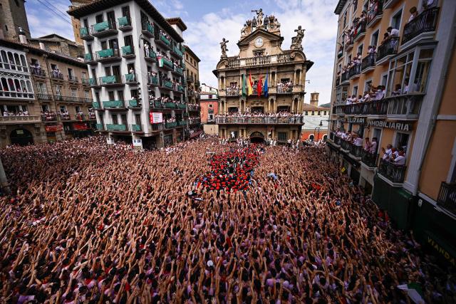 The "Pamplonesa" municipal music band performs during the "Chupinazo" (rocket launch) marking the official start of the San Fermin Festival in Plaza Consistorial outside the Town Hall of Pamplona in northern Spain on July 6, 2025. Thousands of people every year attend the week-long festival and its famous 'encierros' (bull runs) in which six bulls are released at 8:00 a.m. evey day starting July 7, to run from their corral to the bullring through the narrow streets of the old town over an 850 meters (yard) course while runners ahead of them try to stay close to the bulls without falling over or being gored. (Photo by ANDER GILLENEA / AFP)