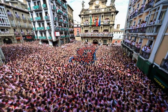 The "Pamplonesa" municipal music band performs during the "Chupinazo" (rocket launch) marking the official start of the San Fermin Festival in Plaza Consistorial outside the Town Hall of Pamplona in northern Spain on July 6, 2025. Thousands of people every year attend the week-long festival and its famous 'encierros' (bull runs) in which six bulls are released at 8:00 a.m. evey day starting July 7, to run from their corral to the bullring through the narrow streets of the old town over an 850 meters (yard) course while runners ahead of them try to stay close to the bulls without falling over or being gored. (Photo by ANDER GILLENEA / AFP)