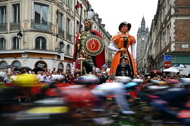The pack of riders (peloton) cycles past "Geants du Nord", giant figurines of northern French folklore, at the start of the 2nd stage of the 112th edition of the Tour de France cycling race, 209.1 km between Lauwin-Planque and Boulogne-sur-Mer, Northern France, on July 6, 2025. (Photo by Loic VENANCE / AFP)