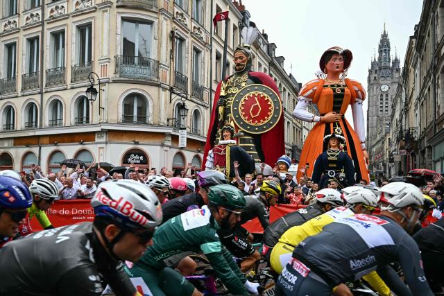 The pack of riders (peloton) cycles past "Geants du Nord", giant figurines of northern French folklore, at the start of the 2nd stage of the 112th edition of the Tour de France cycling race, 209.1 km between Lauwin-Planque and Boulogne-sur-Mer, Northern France, on July 6, 2025. (Photo by Loic VENANCE / AFP)