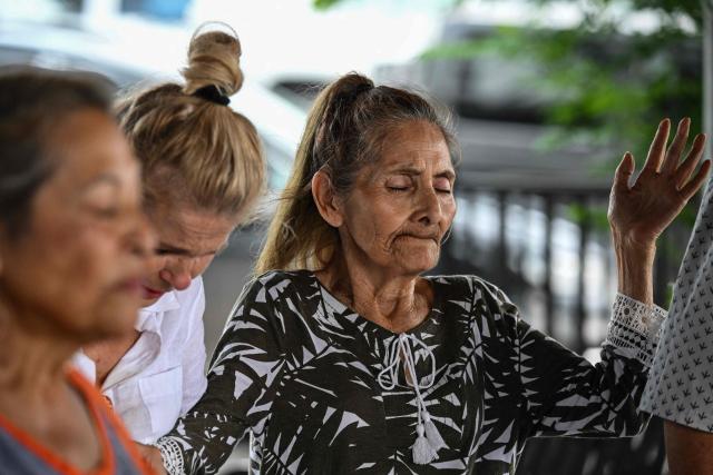People pray near Guadalupe River in Kerrville, Texas, on July 6, 2025, following severe flash flooding that occured during the July 4 holiday weekend. Rescuers in Texas raced against time Sunday to find dozens of missing people, including children, swept away by flash floods that killed at least 78, as forecasters warned of new deluges. Local Texans joined forces with disaster officials to search through the night for the missing, including 27 girls from a riverside Christian summer camp. Texas Governor Greg Abbott said Camp Mystic on the banks of the Guadalupe River, where some 750 girls had been staying when the floodwaters hit, had been "horrendously ravaged in ways unlike I've seen in any natural disaster." (Photo by RONALDO SCHEMIDT / AFP)