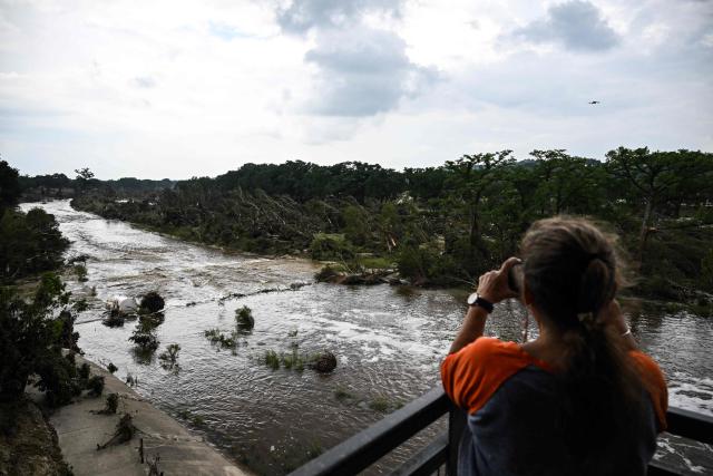 A woman takes pictures of the Guadalupe River in Kerrville, Texas, on July 6, 2025, following severe flash flooding that occured during the July 4 holiday weekend. Rescuers in Texas raced against time Sunday to find dozens of missing people, including children, swept away by flash floods that killed at least 78, as forecasters warned of new deluges. Local Texans joined forces with disaster officials to search through the night for the missing, including 27 girls from a riverside Christian summer camp. Texas Governor Greg Abbott said Camp Mystic on the banks of the Guadalupe River, where some 750 girls had been staying when the floodwaters hit, had been "horrendously ravaged in ways unlike I've seen in any natural disaster." (Photo by RONALDO SCHEMIDT / AFP)