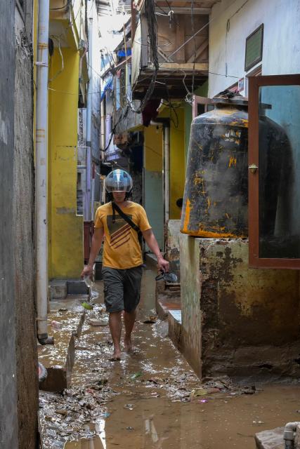 A man walks through a muddy alley after floods hit her neighbourhood following heavy rainfall in Jakarta on July 7, 2025. (Photo by BAY ISMOYO / AFP)