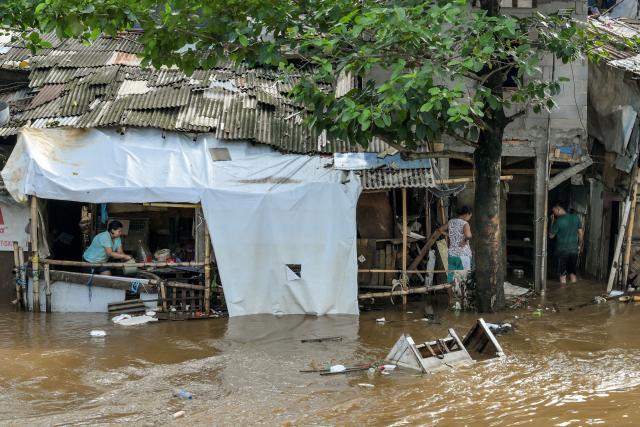 A woman (L) attempts to drain water from inside her home as floods hit her neighbourhood following heavy rainfall in Jakarta on July 7, 2025. (Photo by BAY ISMOYO / AFP)