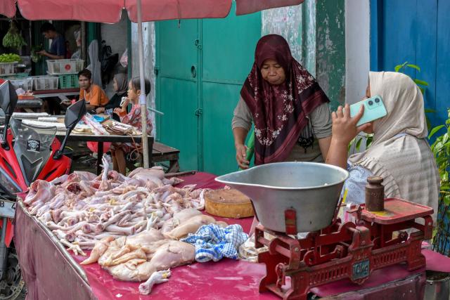 A chicken vendor uses her mobile phone as she waits for customers at a roadside stall in Jakarta on July 7, 2025. (Photo by BAY ISMOYO / AFP)