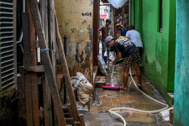 Residents clean muddy alleys in front of their homes after floods swept through their neighbourhood following heavy rainfall in Jakarta on July 7, 2025. (Photo by BAY ISMOYO / AFP)