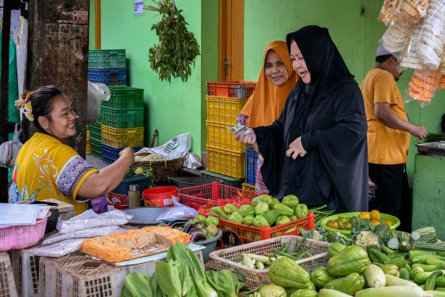 A customer pays for her groceries at a roadside vegetable stall in Jakarta on July 7, 2025. (Photo by BAY ISMOYO / AFP)