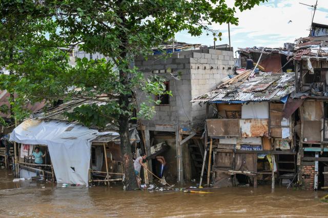 Residents whose homes were flooded try to fend off garbage entering their shanty houses following heavy rainfall in Jakarta on July 7, 2025. (Photo by BAY ISMOYO / AFP)