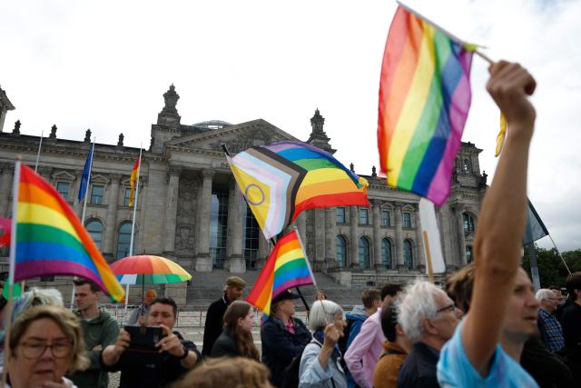 Demonstrators wave rainbow flags as they protest in an LGBTQ+ action titled "Show the flag: For queer visibility in the Bundestag!" on July 8, 2025 in front of the Reichstag building that houses the Bundestag (lower house of parliament) in Berlin, prior to a general debate at the parliament and ahead of the Christopher Street Day (CSD) pride march to take place on July 26, 2025 in the German capital. (Photo by Odd ANDERSEN / AFP)