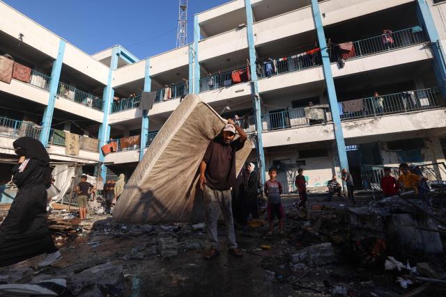 A Palestinian man carries a mattress after an Israeli strike which hit a school sheltering displaced Palestinians in the Al-Bureij camp in the central Gaza Strip on July 8, 2025. A third day of indirect negotiations on a Gaza ceasefire between Israel and Palestinian Islamist movement Hamas began in Doha on July 8, a Palestinian source close to the talks said. (Photo by Eyad BABA / AFP)