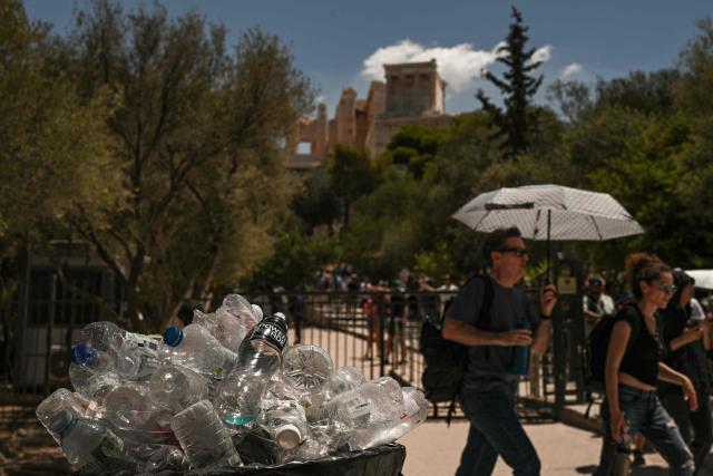 Tourists walk past a rubbish bin overflowing with plastic bottles near Acropolis Hill in Athens on July 8, 2025. Greece's top archaeological monument, The Acropolis, was partially shut as part of emergency measures to protect visitors and workers around the country during a four-day heatwave. The four-day heatwave confirmed by meteorologists began July 6, is the second to grip Greece since late June. Temperatures are expected to reach 42 Celsius (107.6 Fahrenheit), with a maximum of 38 Celsius in Athens and increase as the week continues. (Photo by Aris MESSINIS / AFP)