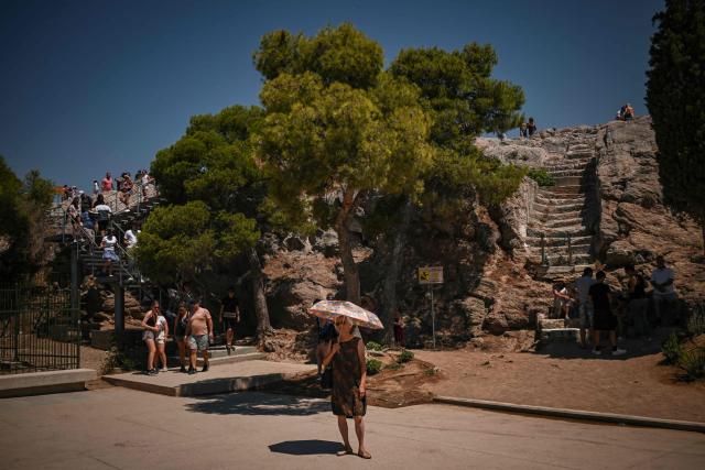 A tourist holds an umbrella as she stands opposite Acropolis Hill in Athens on July 8, 2025. Greece's top archaeological monument, The Acropolis, was partially shut as part of emergency measures to protect visitors and workers around the country during a four-day heatwave. The four-day heatwave confirmed by meteorologists began July 6, is the second to grip Greece since late June. Temperatures are expected to reach 42 Celsius (107.6 Fahrenheit), with a maximum of 38 Celsius in Athens and increase as the week continues. (Photo by Aris MESSINIS / AFP)
