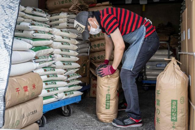 A member of staff works as bags of rice are seen piled up at a rice store in Tokyo on July 9, 2025. While US President Donald Trump imposed a 10 percent tariff on most US trading partners in April, the rate is set to rise for dozens of economies including the European Union and Japan come July 9. (Photo by Yuichi YAMAZAKI / AFP)