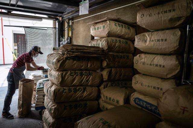 A member of staff works as bags of rice are seen piled up at a rice store in Tokyo on July 9, 2025. While US President Donald Trump imposed a 10 percent tariff on most US trading partners in April, the rate is set to rise for dozens of economies including the European Union and Japan come July 9. (Photo by Yuichi YAMAZAKI / AFP)
