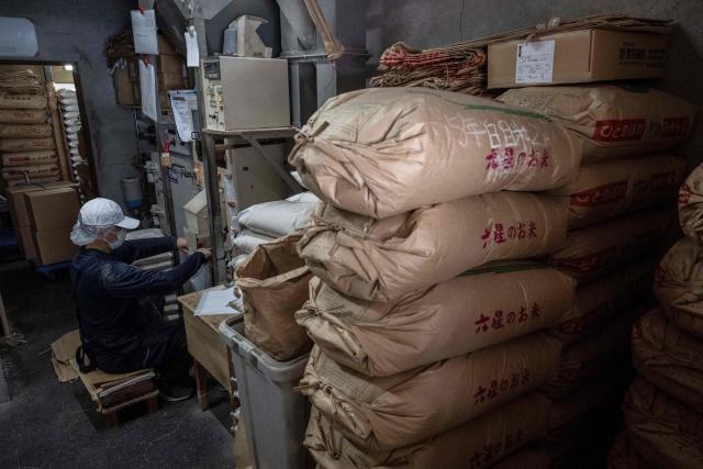 A member of staff works as bags of rice are seen piled up at a rice store in Tokyo on July 9, 2025. While US President Donald Trump imposed a 10 percent tariff on most US trading partners in April, the rate is set to rise for dozens of economies including the European Union and Japan come July 9. (Photo by Yuichi YAMAZAKI / AFP)