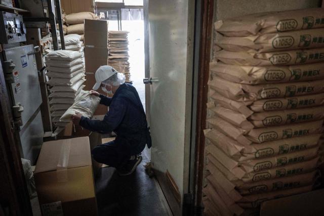 A member of staff works as bags of rice are seen piled up at a rice store in Tokyo on July 9, 2025. While US President Donald Trump imposed a 10 percent tariff on most US trading partners in April, the rate is set to rise for dozens of economies including the European Union and Japan come July 9. (Photo by Yuichi YAMAZAKI / AFP)