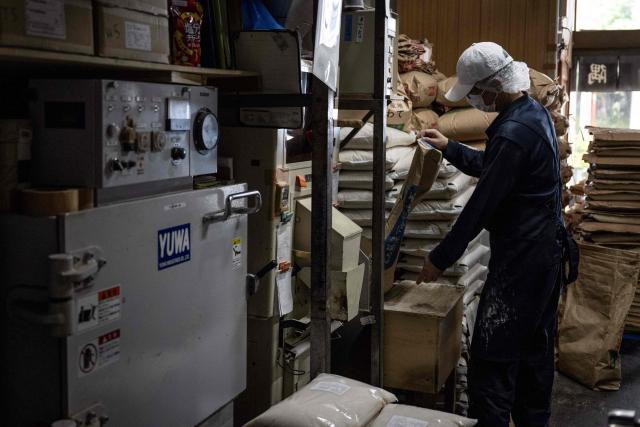 A member of staff works as bags of rice are seen piled up at a rice store in Tokyo on July 9, 2025. While US President Donald Trump imposed a 10 percent tariff on most US trading partners in April, the rate is set to rise for dozens of economies including the European Union and Japan come July 9. (Photo by Yuichi YAMAZAKI / AFP)