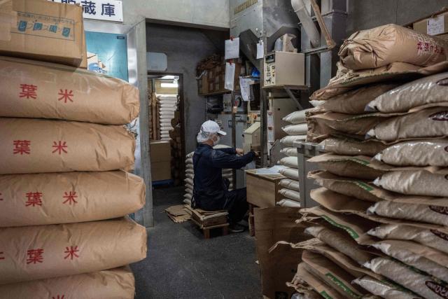 A member of staff works as bags of rice are seen piled up at a rice store in Tokyo on July 9, 2025. While US President Donald Trump imposed a 10 percent tariff on most US trading partners in April, the rate is set to rise for dozens of economies including the European Union and Japan come July 9. (Photo by Yuichi YAMAZAKI / AFP)