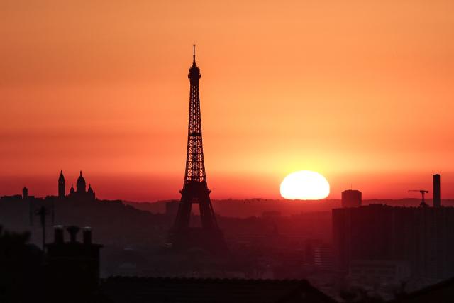 (FILES) The sun rises by the Eiffel Tower and the Sacre Coeur Basilica ontop of the Montmartre hill in Paris on July 1, 2025, as the city is on red alert for high temperatures, with the top of the Eiffel Tower shut, polluting traffic banned and speed restrictions in place as a searing heatwave gripped Europe. Human-caused climate change made the recent European heatwave up to 4C hotter in many cities, scientists said on July 9, 2025, pushing temperatures into deadly territory for thousands of vulnerable people. (Photo by Thibaud MORITZ / AFP)
