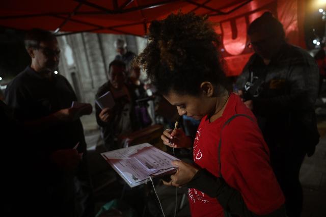 A woman signs a public petition to end the six-day workweek during a demonstration calling to tax the super-rich and demanding the end of the six-day workweek in Rio de Janeiro, Brazil, on July 10, 2025. The reduction of the workweek to six days started as a popular demand and is now gaining support among politicians. Additionally, the Brazilian federal government has presented a bill proposing a 10% tax on the super-rich, which is currently under discussion in Congress. (Photo by MAURO PIMENTEL / AFP)