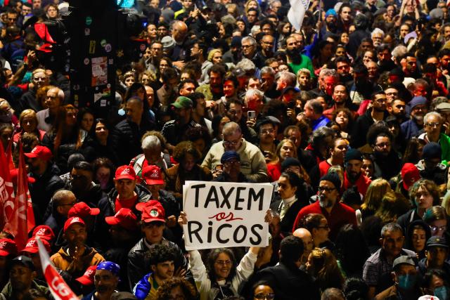 People attend a demonstration calling to tax the super-rich and demanding the end of the six-day workweek at the Paulista Avenue in Sao Paulo, Brazil, on July 10, 2025. The reduction of the workweek to six days started as a popular demand and is now gaining support among politicians. Additionally, the Brazilian federal government has presented a bill proposing a 10% tax on the super-rich, which is currently under discussion in Congress. (Photo by Miguel SCHINCARIOL / AFP)