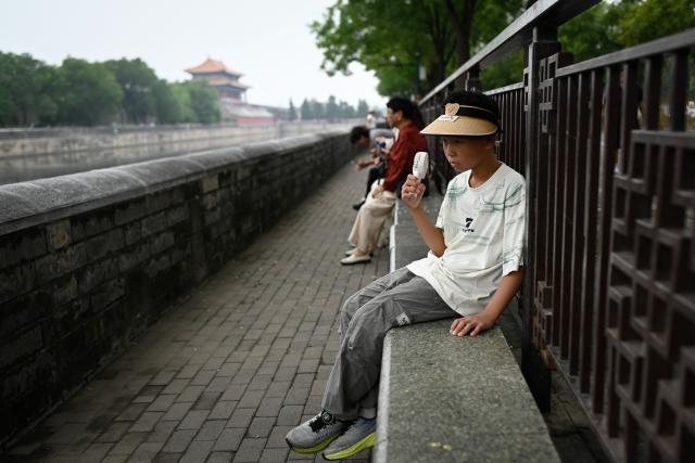 A child uses a mini fan for cooling outside the Forbidden City in Beijing on July 11, 2025. (Photo by WANG Zhao / AFP)