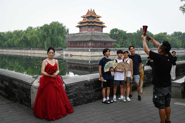A woman wearing a wedding dress stands next a family taking a group photo near the Forbidden City in Beijing on July 11, 2025. (Photo by WANG Zhao / AFP)