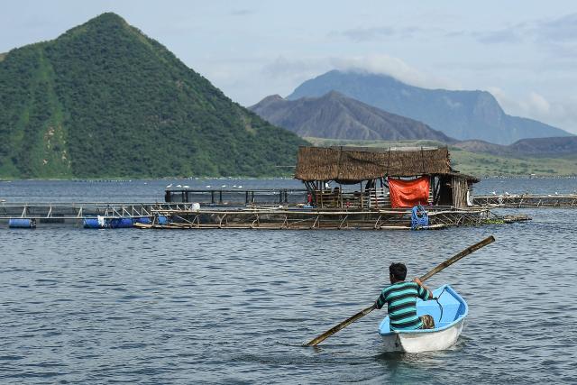 A worker sails his wooden boat near fish cages at the foot of the Taal volcano crater along Taal Lake off Laurel town, Batangas province, south of Manila, on July 10, 2025. (Photo by Ted ALJIBE / AFP)
