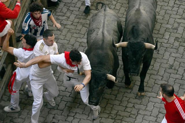 Participants try to dodge the Jose Escolar breed bulls during the sixth running of the bulls of the San Fermin festival in Pamplona, northern Spain, on July 12, 2025. Thousands of people every year attend the week-long festival and its famous "encierros" or bull runs, every day at 8:00 a.m. through the narrow streets of the old town over an 850 meters (yard) course while runners ahead of them try to stay close to the bulls without falling over or being gored. (Photo by ANDER GILLENEA / AFP)