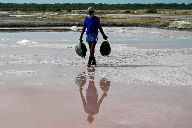A salt farmer collects sea salt at an alkali flat, near a beach in Karachi on July 12, 2025. (Photo by Rizwan TABASSUM / AFP)