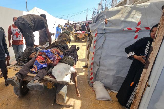 EDITORS NOTE: Graphic content / A woman looks on as Palestinians transport the bodies of victims to a Red Cross clinic in Rafah in the southern Gaza Strip after they were reportedly shot as they waited to receive food parcels at a distribution point run by the US and Israel-backed Gaza Humanitarian Foundation (GHF), on July 12, 2025. Gaza's civil defence agency said at least 14 Palestinians were killed in the latest wave of Israeli strikes across the territory on July 12. (Photo by AFP)