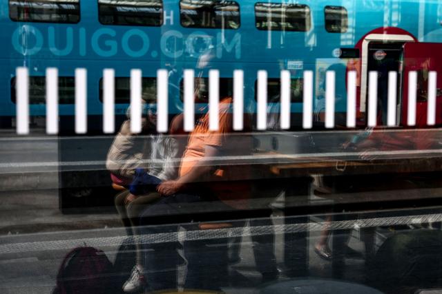People siting in a hall are reflected beside a Ouigo train at the gare de Lyon train station in Paris on July 12, 2025. (Photo by Guillaume BAPTISTE / AFP)