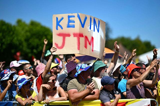 Spectators cheer, with a placard supporting Arkea-B&B Hotels team's French rider Kevin Vauquelin at the start of the 8th stage of the 112th edition of the Tour de France cycling race, 171.4 km between Saint-Meen-le-Grand and Laval Espace Mayenne, western France, on July 12, 2025. (Photo by Loic VENANCE / AFP)
