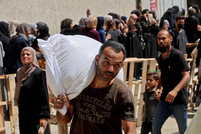 A Palestinian man carries a bag of flower at a UN World Food Programme (WFP) warehouse on Al-Jalaa street in Gaza City, in the central Gaza Strip on July 12, 2025. Indirect talks between Hamas and Israel for a ceasefire in Gaza are being held up by Israel's proposals to keep troops in the territory, two Palestinian sources with knowledge of the discussions told AFP on July 12. (Photo by Omar AL-QATTAA / AFP)
