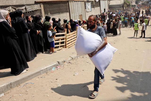 A Palestinian man carries a bag of flour outside a UN World Food Programme (WFP) warehouse on Al-Jalaa street in Gaza City, in the central Gaza Strip on July 12, 2025. Indirect talks between Hamas and Israel for a ceasefire in Gaza are being held up by Israel's proposals to keep troops in the territory, two Palestinian sources with knowledge of the discussions told AFP on July 12. (Photo by Omar AL-QATTAA / AFP)